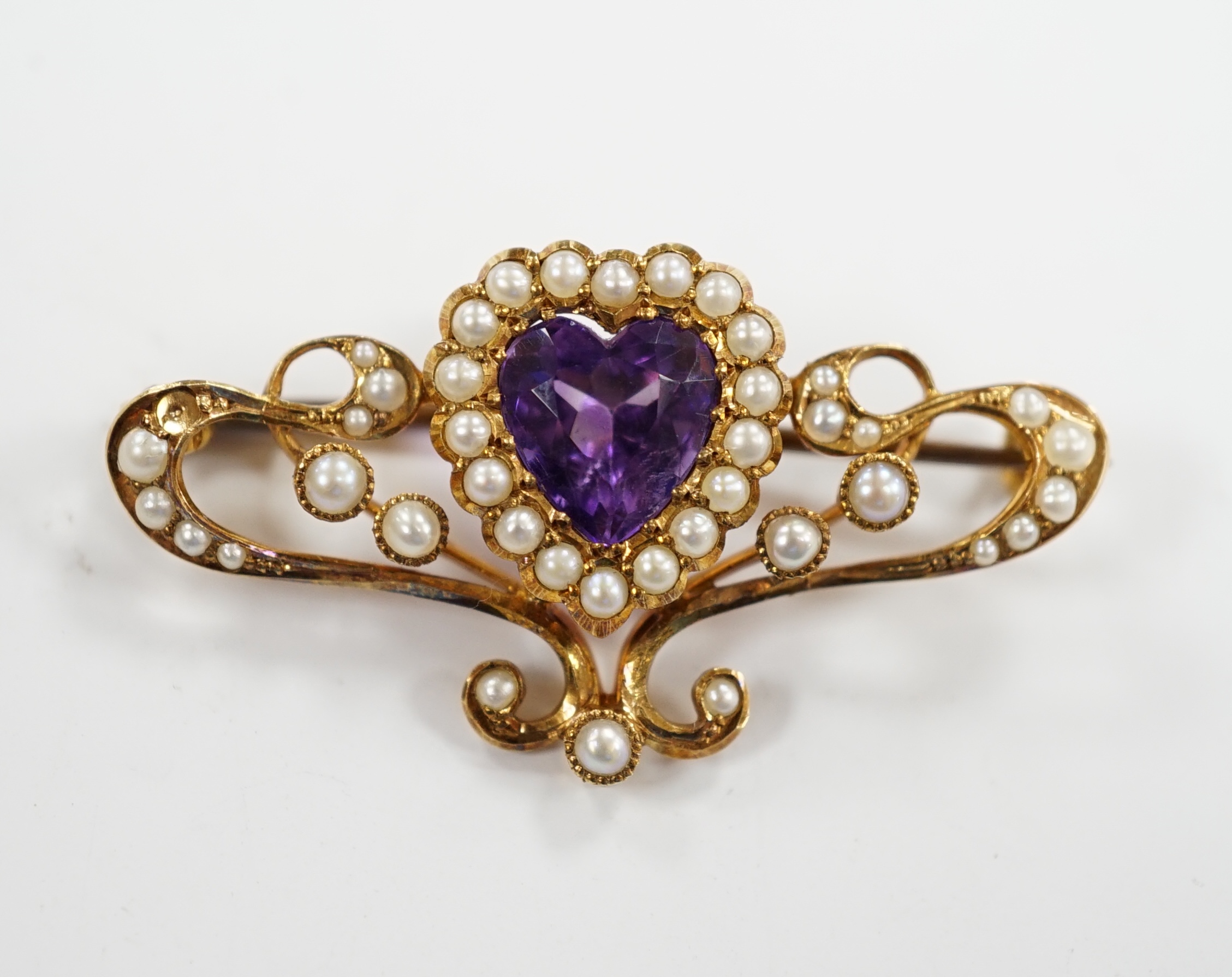 An Edwardian 15ct?, amethyst and seed pearl cluster set bar brooch, with central heart motif, 38mm, gross weight 4.7 grams.